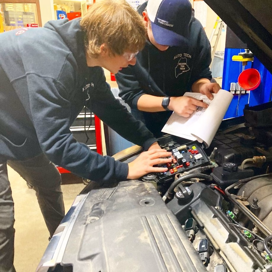 Two auto tech students under hood diagnose car issues